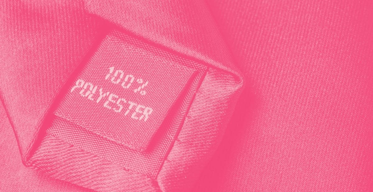 Close-up of a pink fabric label reading "HERSCHEL 100% POLYESTER" sewn onto a textured pink textile.