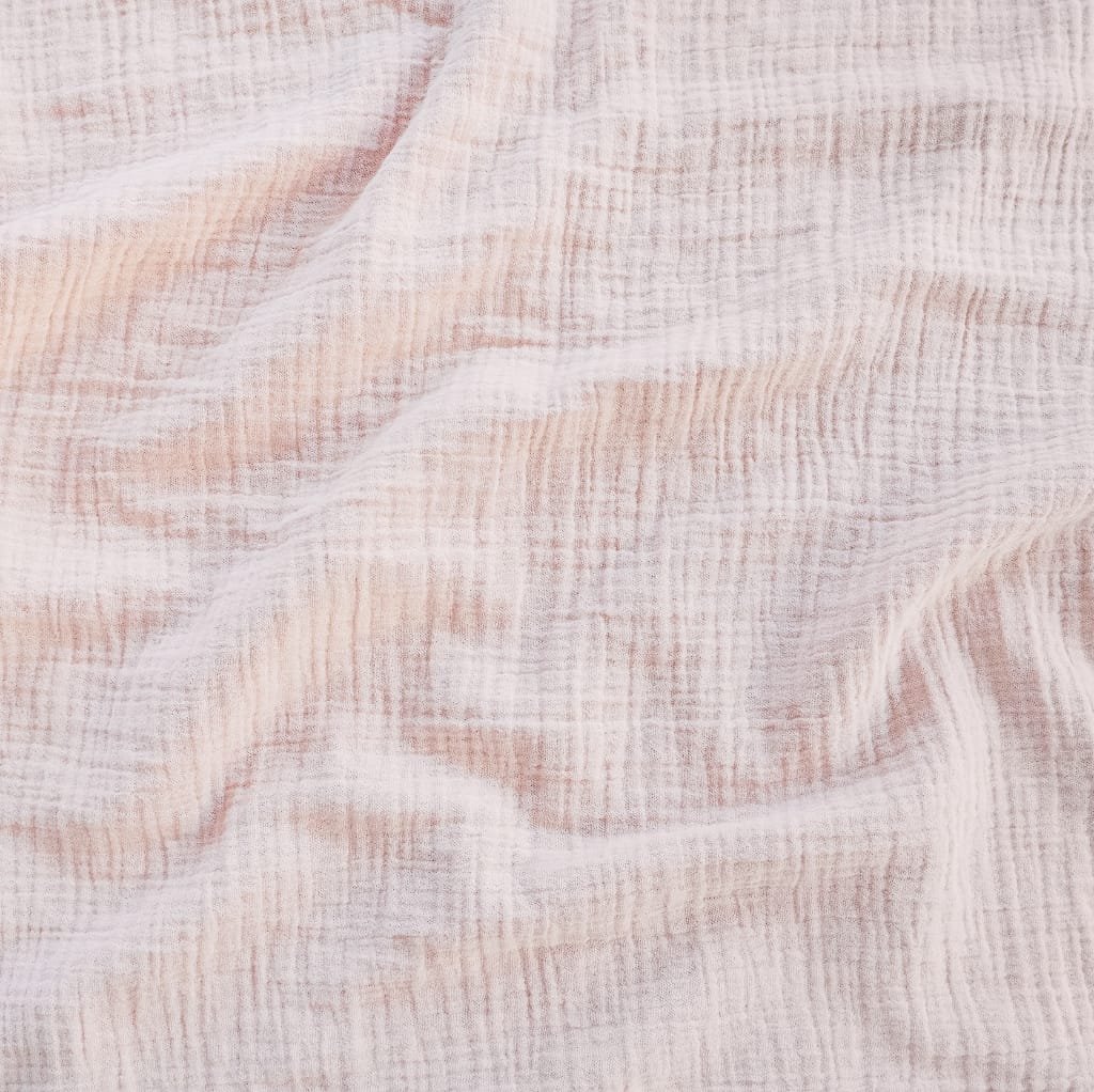 Close-up image of soft, lightweight cotton muslin fabric with gentle folds, showcasing its fine weave and delicate texture in light pink and white tones.