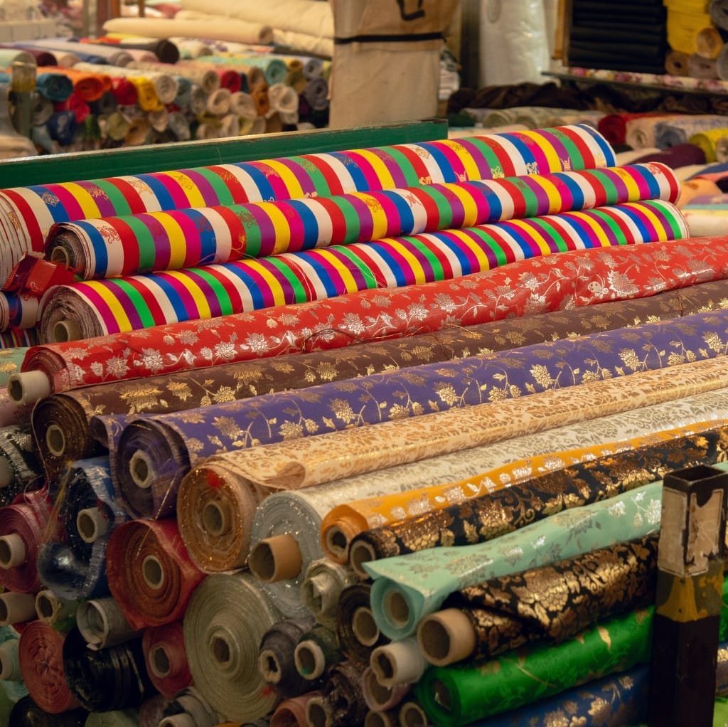 A colorful display of cotton fabric rolls with various patterns and designs stacked on top of each other at a fabric market.