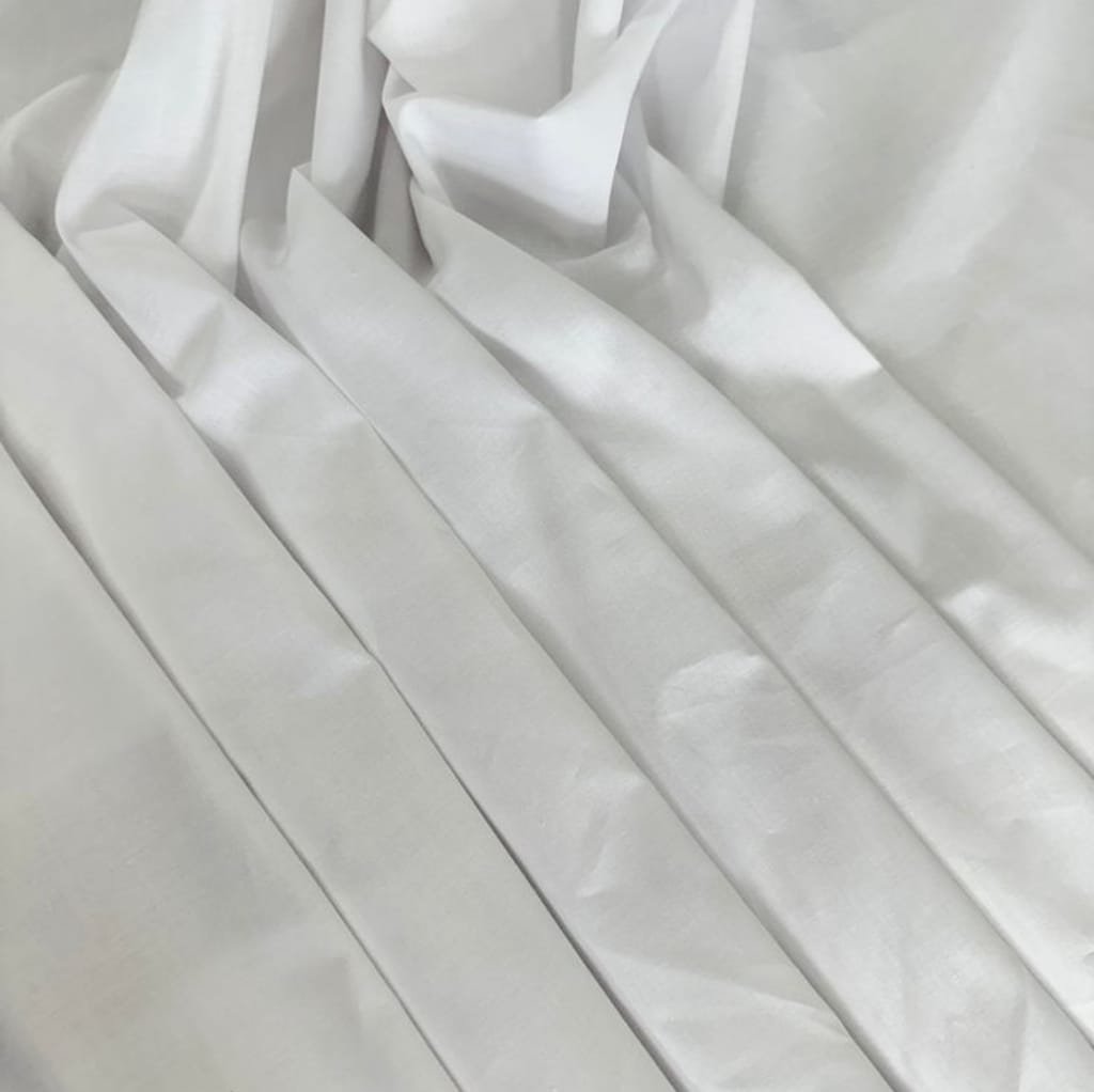 Close-up image of smooth, white cotton fabric with gentle pleats, showcasing a soft and lightweight texture.