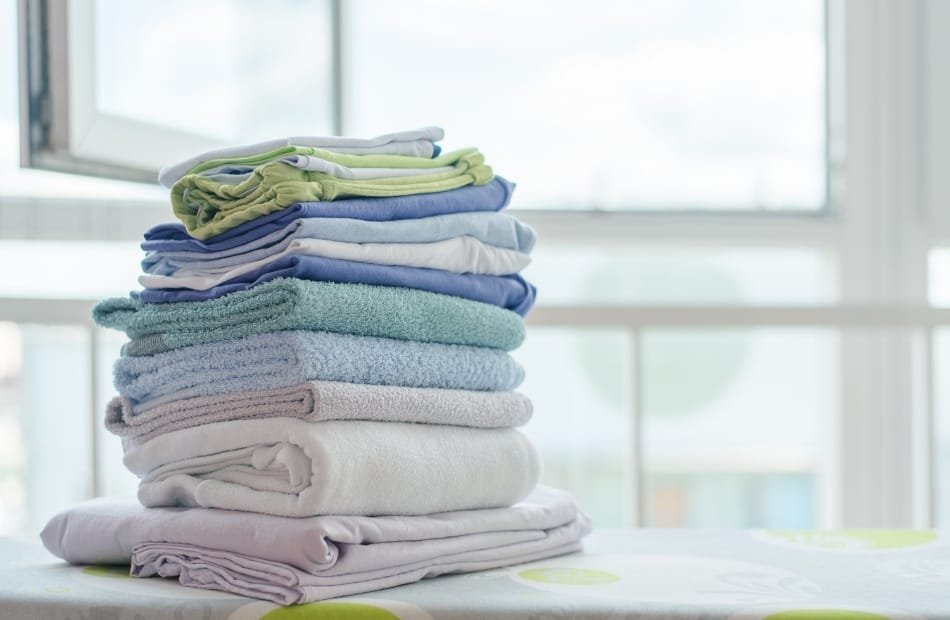 A neatly folded stack of clothes on a table near a window, with the background showcasing bright natural light.