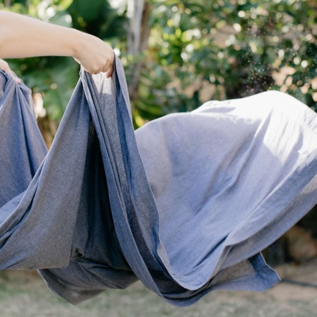 A person holding a pair of jeans in an outdoor setting, with greenery in the background and sunlight filtering through the trees.