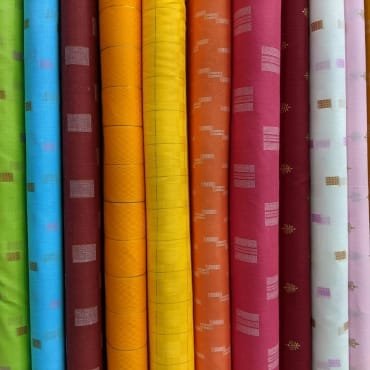 A row of colorful fabric rolls with various vibrant colors and patterns, including shades of blue, red, yellow, orange, pink, and white, showing diverse design options.