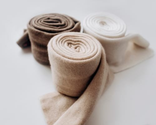 Three rolled pieces of soft, neutral-colored cotton fabric laid out on a white surface, showcasing their smooth texture.