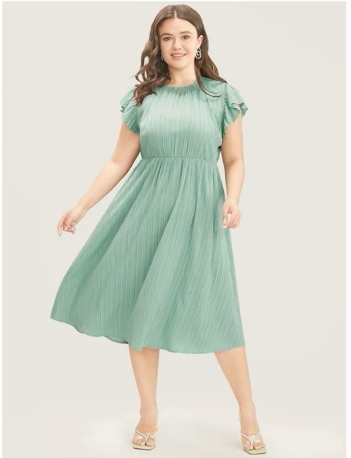 A woman wearing a mint green cotton babydoll dress with ruffled sleeves, standing against a plain background.