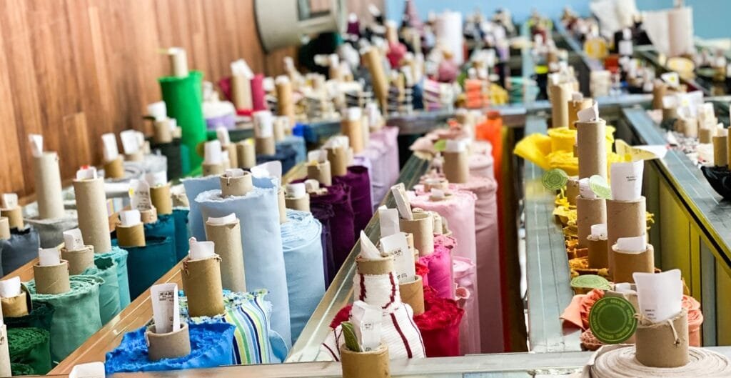A colorful display of cotto fabric rolls arranged on a glass counter at a wholesale fabric market.