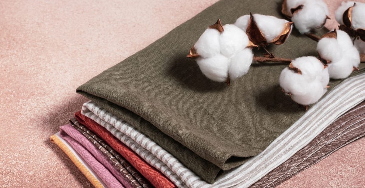 A stack of neatly folded fabrics in various patterns and colors, topped with cotton branches.