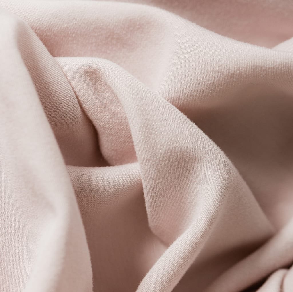 A close-up image of soft, pale pink cotton fabric with gentle folds and smooth texture.