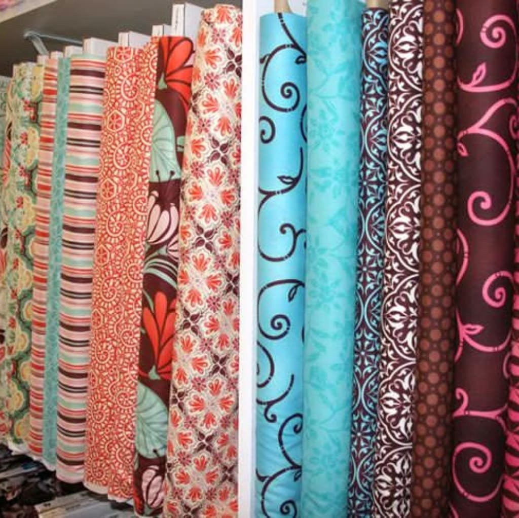 A display of colorful fabric rolls with various intricate patterns and designs, showcasing custom printed cotton fabric rolls in a fabric store.