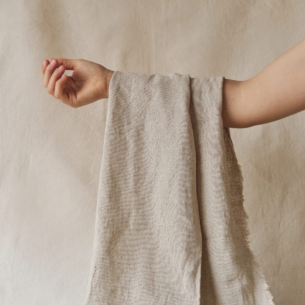 A person holding a beige, textured fabric, with their arm extended against a neutral background.