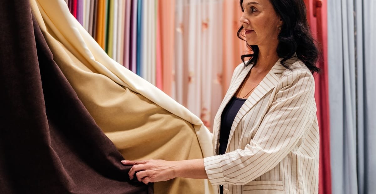Woman examining different drapery fabric types in a curtain showroom.