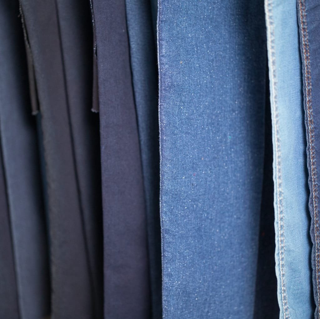 Close-up of several denim fabrics hanging on a rack, showcasing various shades of blue and different textures.