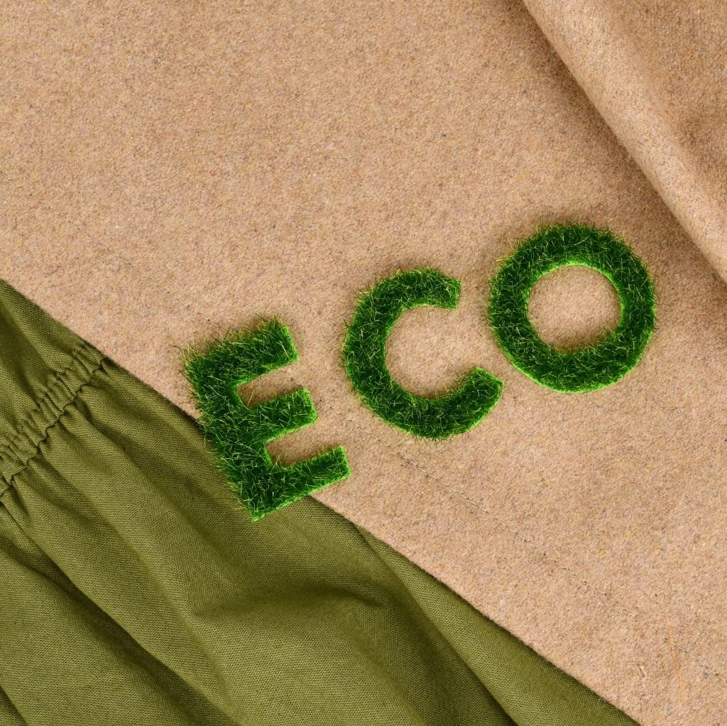 Green fuzzy letters spelling "ECO" placed on a beige textured surface with a green fabric in the bottom left corner.