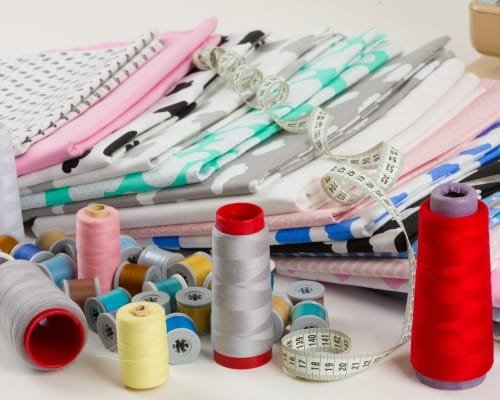 A collection of sewing supplies including colorful spools of thread, neatly folded fabric in pastel shades, and measuring tapes.