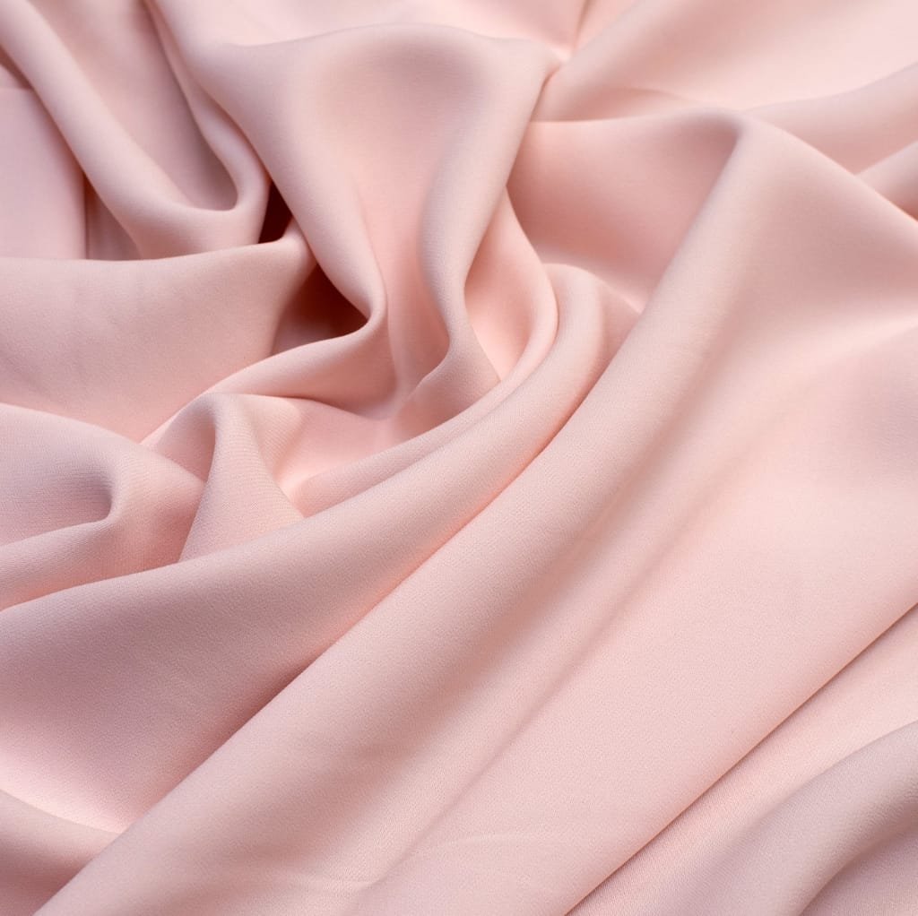 A close-up image of soft, light pink cotton fabric with gentle folds and smooth texture.