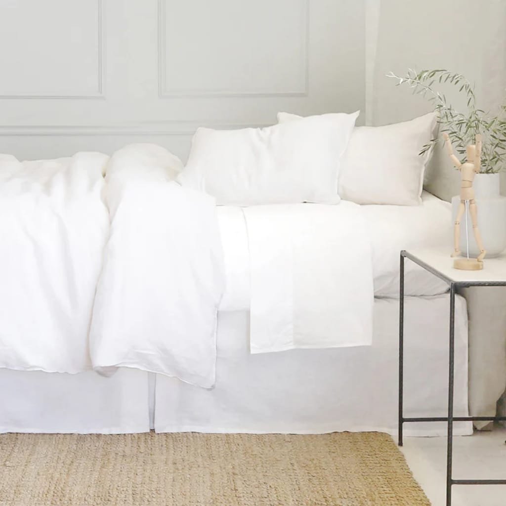Close-up of a bed with white bedding decorated with small black floral patterns, slightly wrinkled with soft natural light.