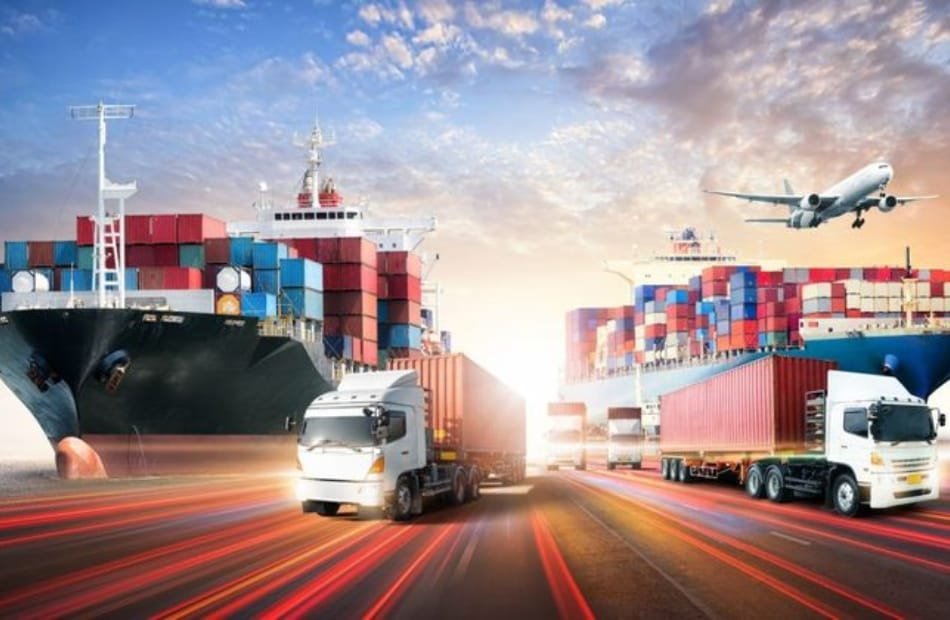 A busy transportation scene showing a large cargo ship, multiple trucks, and an airplane, symbolizing the interconnected logistics and supply chain network involved in cotton trade, with a sunset sky in the background.  How American Cotton Manufacturers 