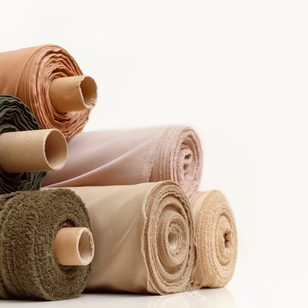 A close-up image of several cotton fabric rolls in various colors, stacked horizontally on a white surface.