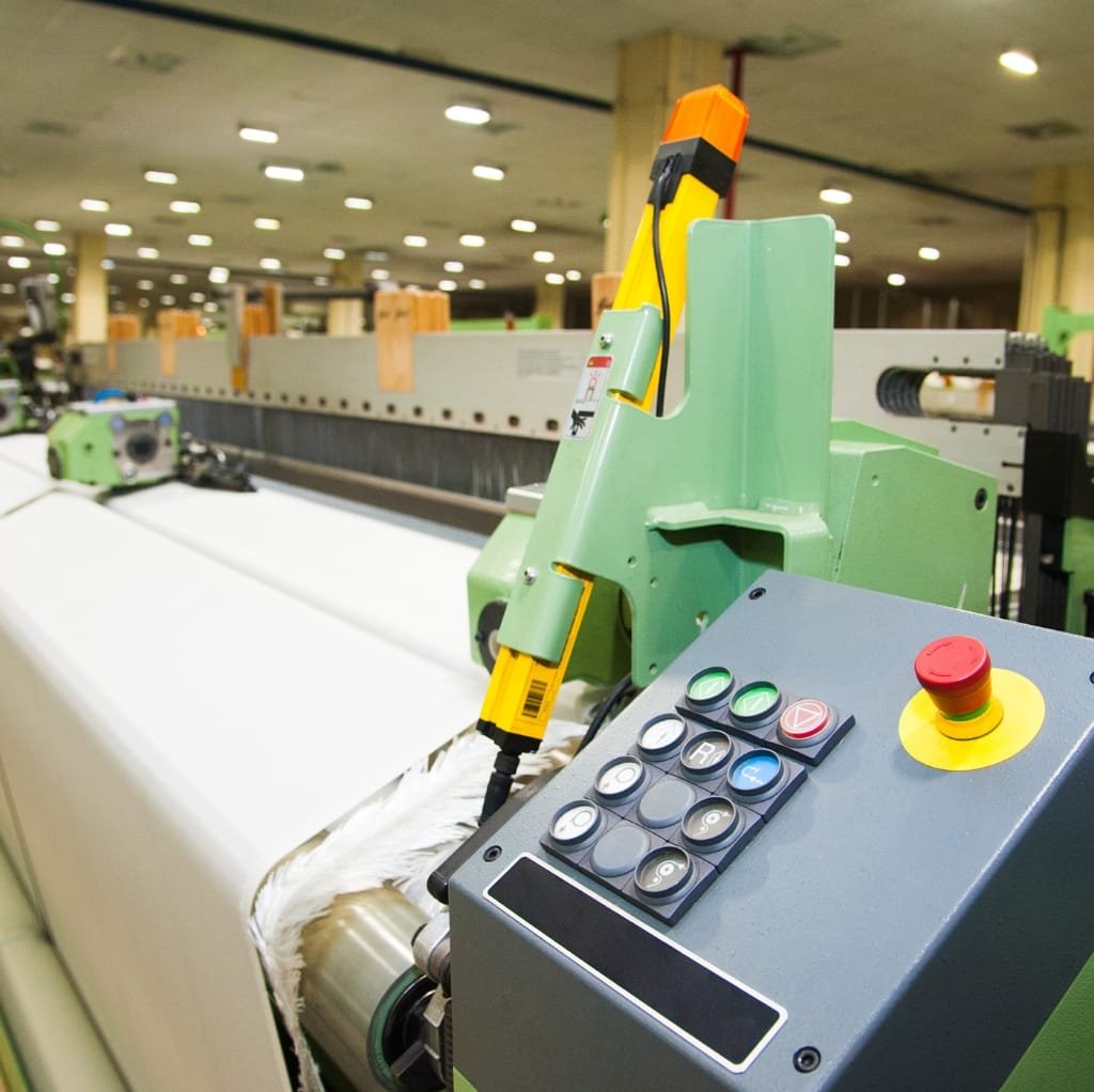 Close-up image of industrial machinery used in fabric production, with buttons and control panel in focus, situated in a factory setting.
