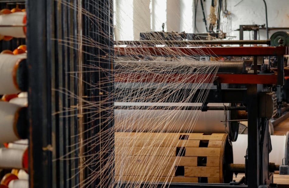 Close-up of textile manufacturing machinery weaving multiple threads, showcasing modern technology in American textile production. American Made Textiles