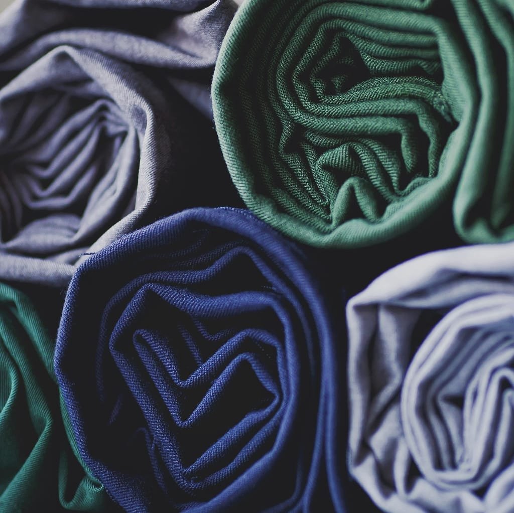 Close-up image of multiple rolled fabric pieces in various colors, including green, navy, gray, and white.