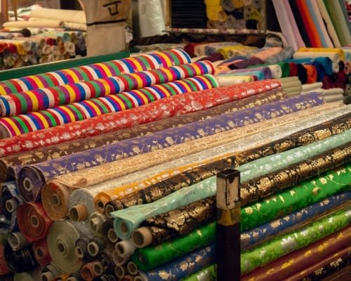 A colorful display of various rolls of patterned and plain cotton fabric stacked on a table in a fabric store.