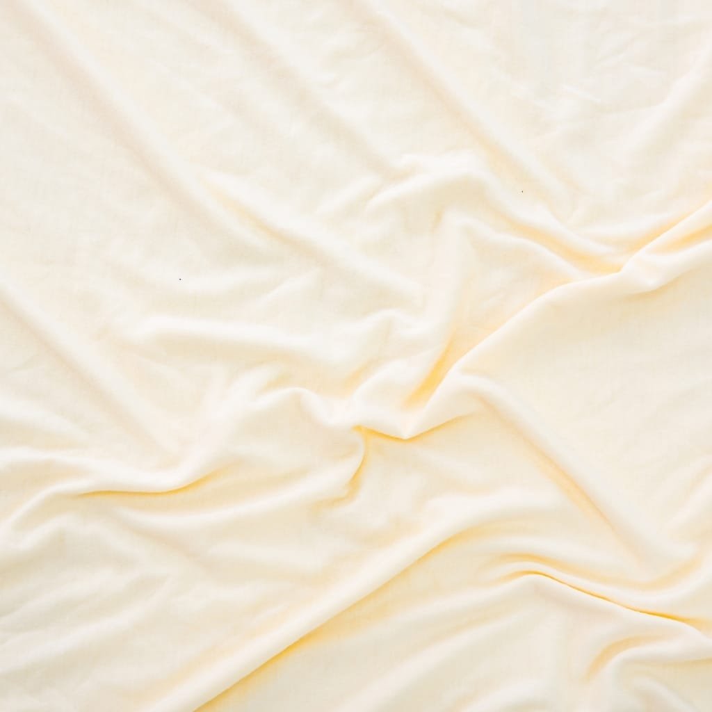 A close-up of soft, cream-colored satin fabric with gentle folds and a smooth, shiny texture.
