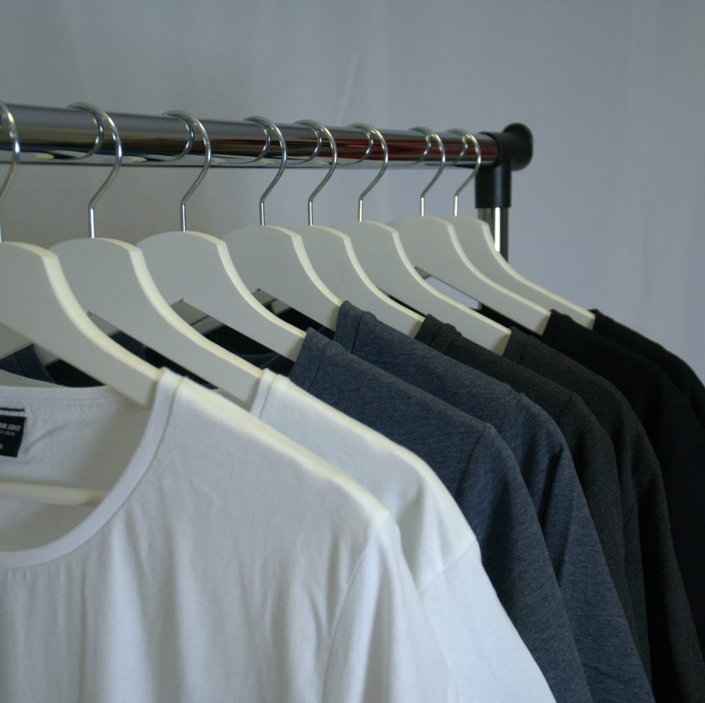 A row of white, gray, and black cotton t-shirts hanging on white hangers on a clothing rack against a neutral background, highlighting summer moisture-absorbing apparel.