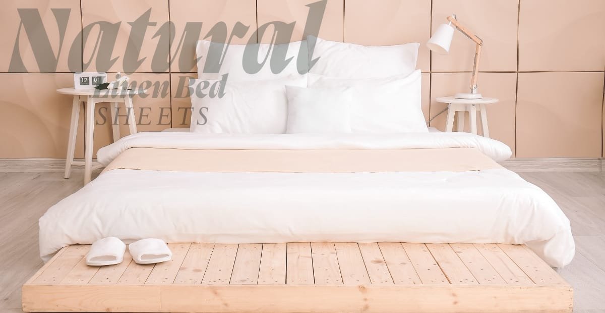 A neatly made bed with white linens and pillows, set against a beige paneled wall. Two matching white bedside tables with lamps are on either side of the bed. There is a light wooden pallet at the foot of the bed with a pair of white slippers placed on it. Overlaid text reads "Natural Linen Bed SHEETS."