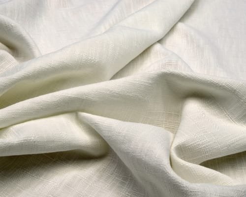 Cream-colored, soft, textured organic cotton fabric with gentle folds and a natural weave. Leading Cotton Fabric Manufacturers