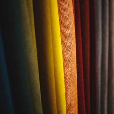 A close-up of vertically hanging fabric swatches in various colors including dark green, yellow, orange, red, and brown.