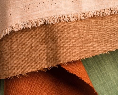 Close-up image of various pieces of fabric in different colors and textures, including pink, orange, green, and brown, showcasing woven textile materials.