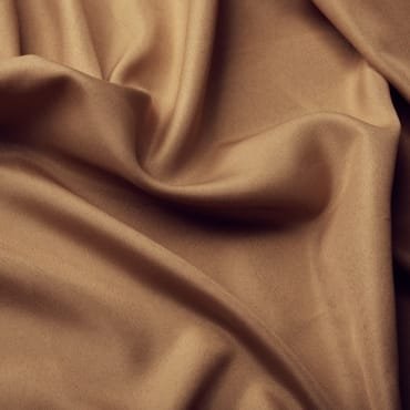 Close-up of smooth, beige polyester fabric with soft folds, ideal for stylish clothing.