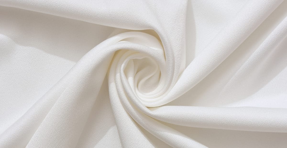 Close-up image of soft, white cotton fabric with a smooth, slightly textured surface, gently twisted in the center.