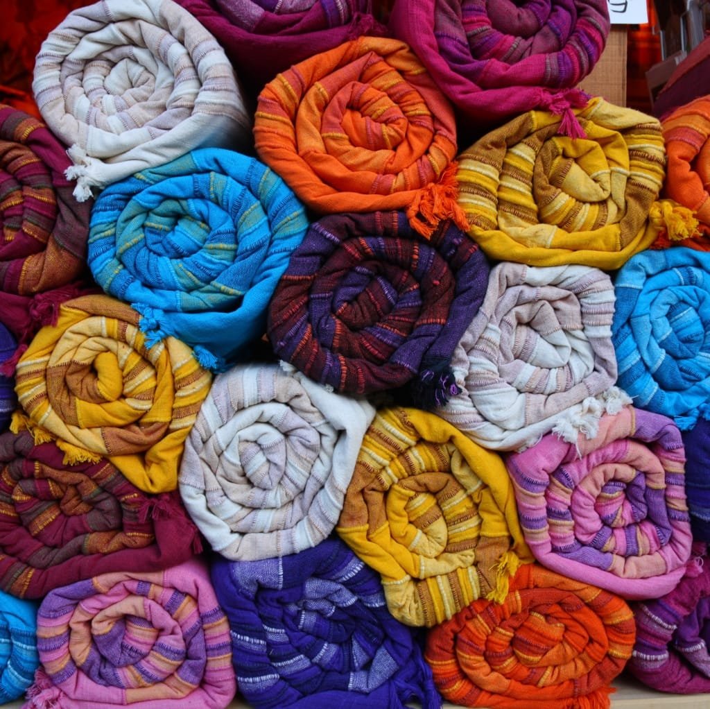 Colorful rolled-up cotton fabrics in various shades, arranged in a piled display.