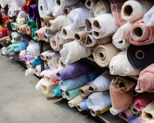 Stacks of colorful fabric rolls stored on shelves in a textile supplier warehouse.
