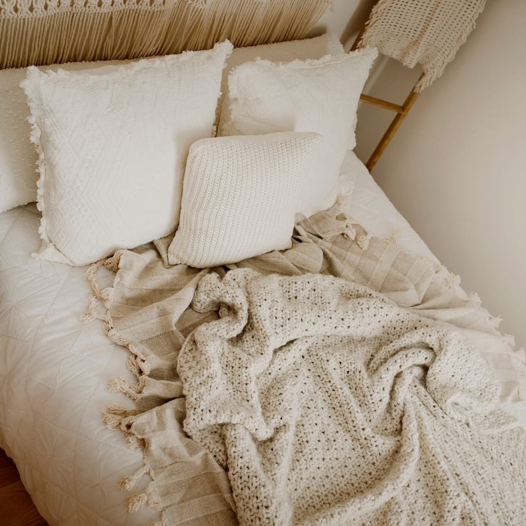 A cozy bedroom bed with white textured pillows, a chunky knit blanket, and neutral-toned bedding, creating a warm and inviting ambiance.