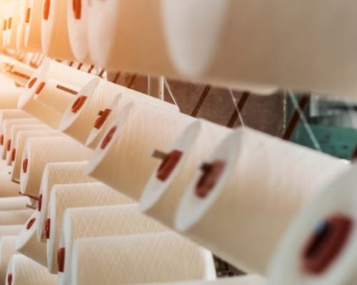 Rows of cotton fabric rolls on a manufacturing conveyor, illuminated with warm lighting, highlighting the texture and quality of the fabric.