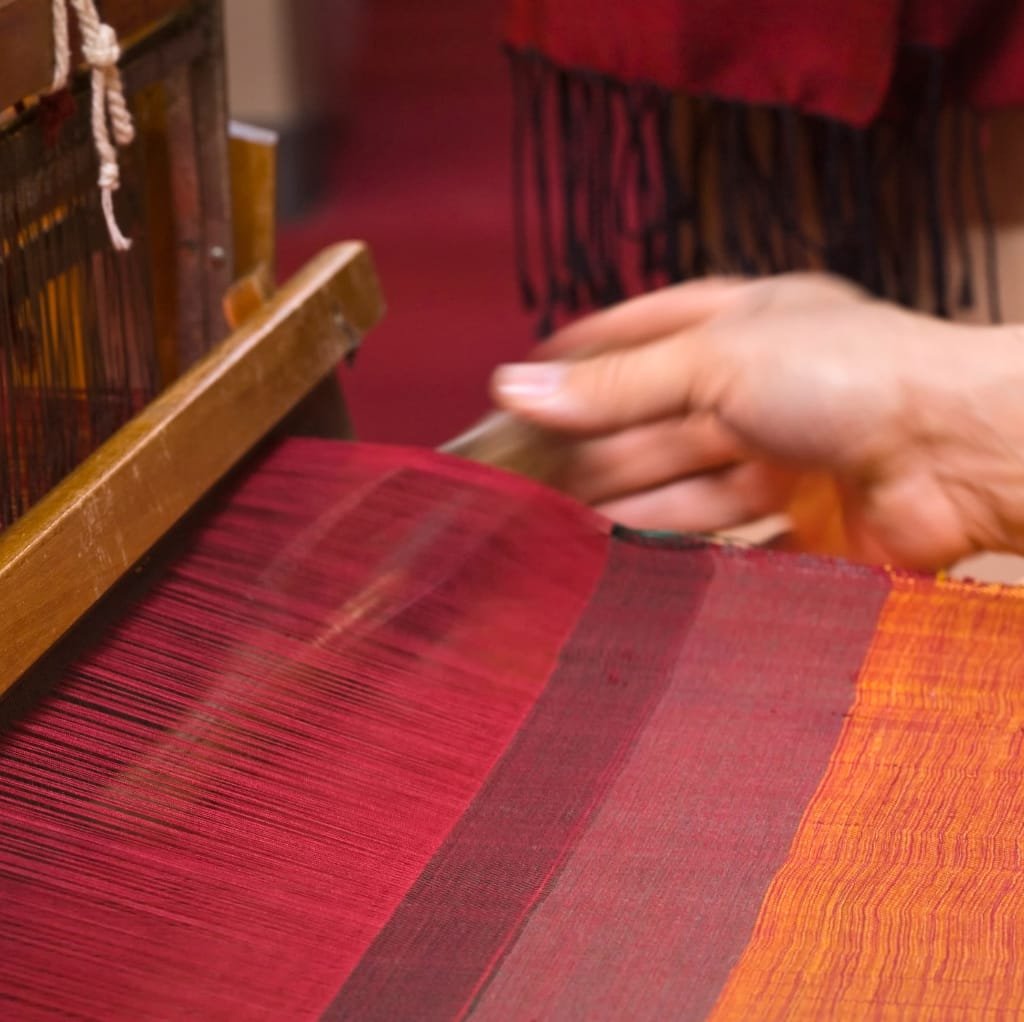 Close-up of hands weaving a vibrant fabric on a loom, showcasing the distinct pattern and texture of twill fabric with red and orange hues.