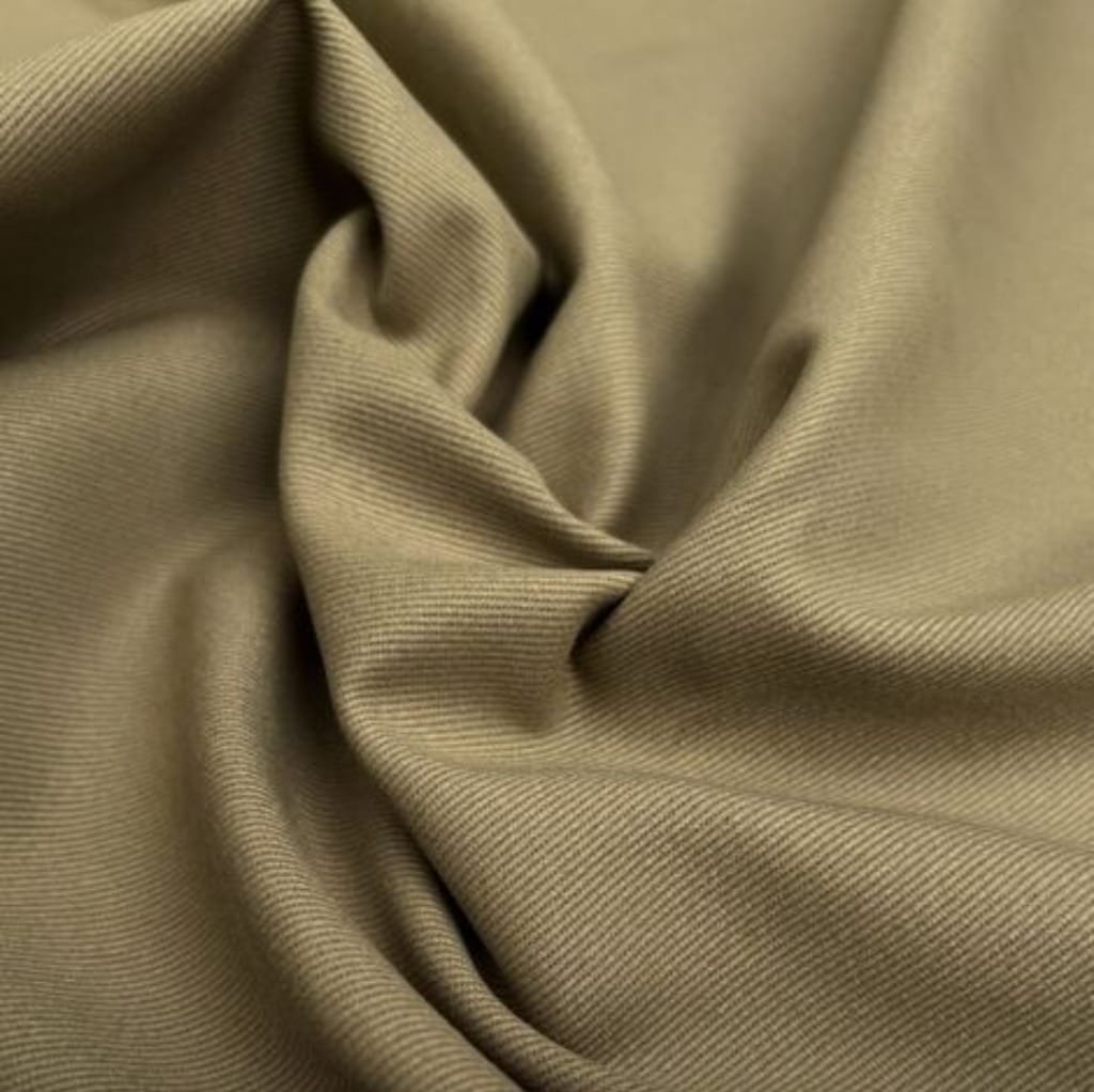 Close-up image of beige twill cotton fabric featuring diagonal weave patterns and soft, smooth texture with gentle folds.