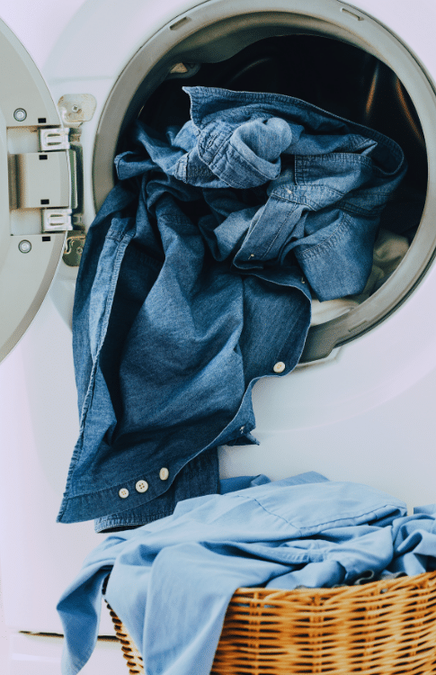 A washing machine with blue jeans spilling out into a laundry basket