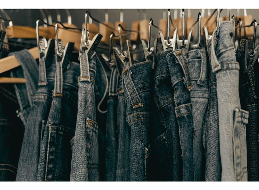 A row of denim jeans hanging on hangers in a clothing store shelf.