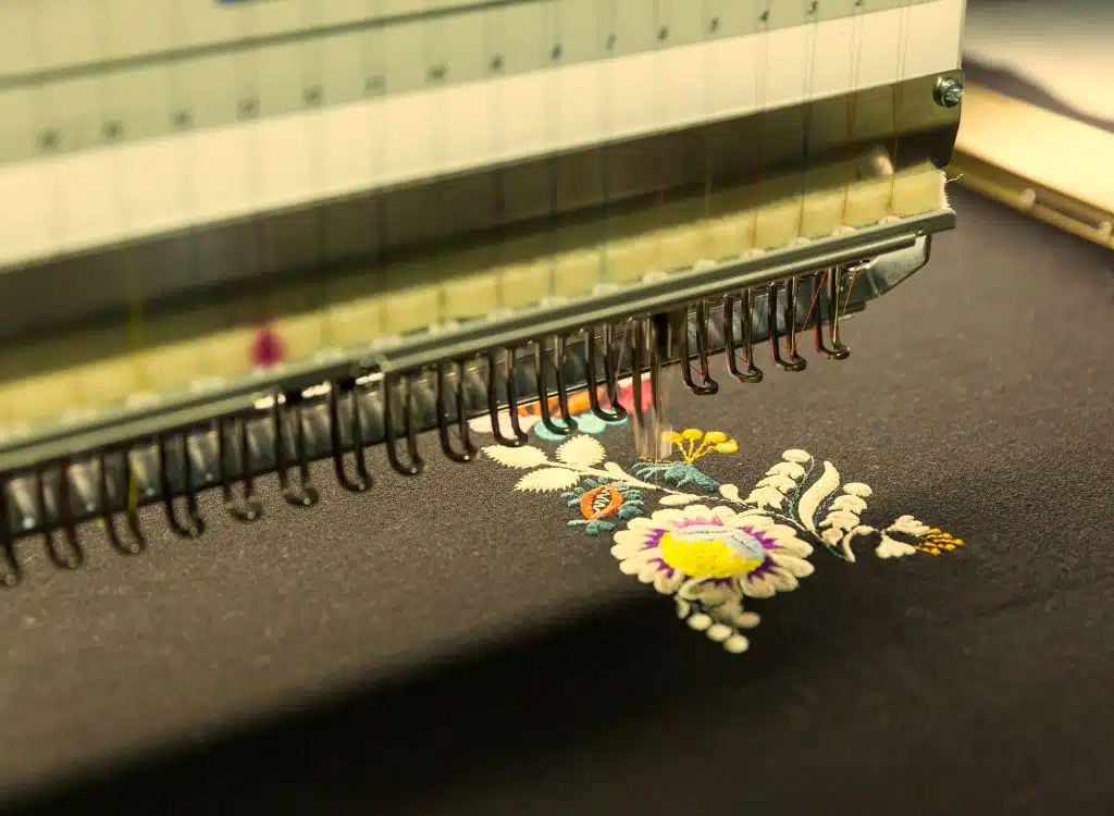 Close-up of an embroidery machine stitching a colorful floral design onto dark fabric, representing clothing manufacturing in Hawaii.