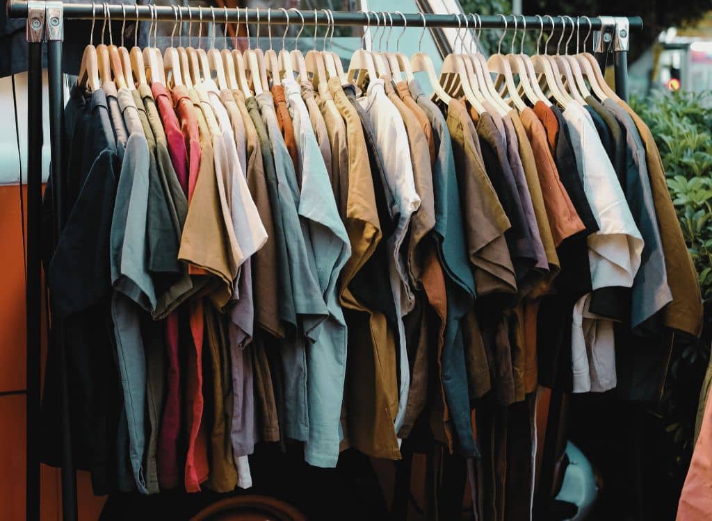 A clothing rack filled with various casual T-shirts and tops in different colors and shades, displayed outdoors.