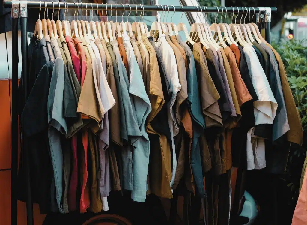 A clothing rack filled with various casual T-shirts and tops in different colors and shades, displayed outdoors.