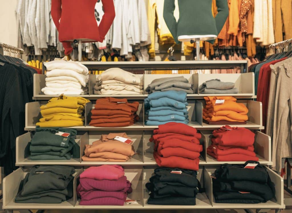 Display of neatly folded sweaters in various colors on a retail store rack.