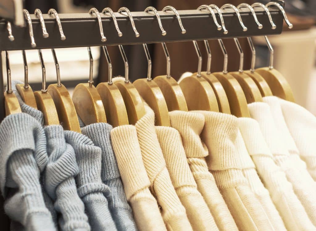 Close-up of neatly hung sweaters on wooden hangers in a clothing store.