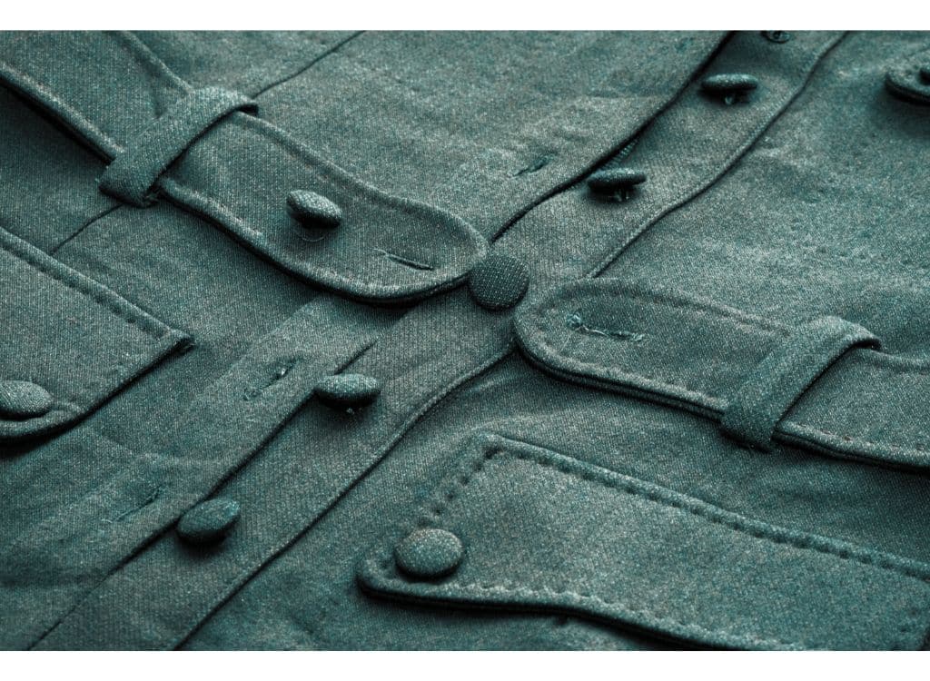 Close-up of a dark green military-style jacket with buttons and pockets, showcasing detailed stitching and fabric texture.