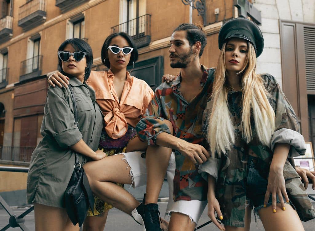 Group of trendy young people wearing stylish clothing and sunglasses, standing outdoors in an urban setting.