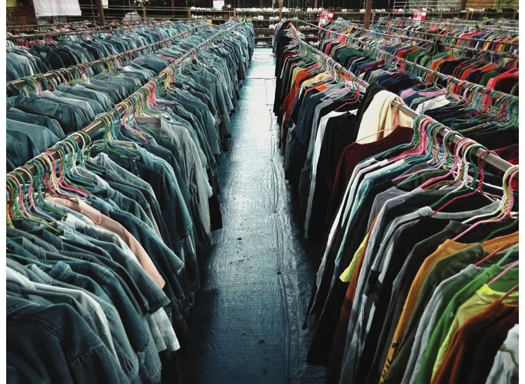 Rows of hanging clothing on racks at a wholesale clothing market or manufacturing facility.